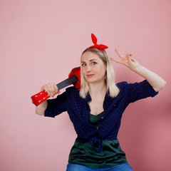 Portrait of  stylish young blonde with ukulele. A woman with a headband on a pink background
