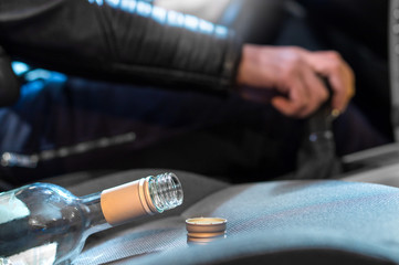 Drunk driving concept. Young man driving car under the influence of alcohol. Hand on gear stick. Close up of empty bottle of wine on front seat. Traffic safety risk.