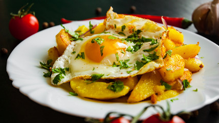 fried egg with potato in a plate on dark wooden background