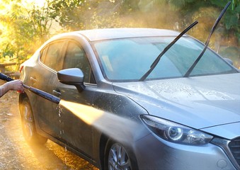 Car Washing. Cleaning grey color car using high pressure water in the morning with sunray