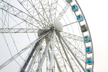 Detail of a large and high Ferris wheel with poles and white irons. The cabins have blue glass and there is none.
