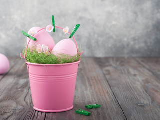 Easter basket (bucket) like nest with grass with cute pink eggs, flowers on grey wooden background. Copy space for your card.