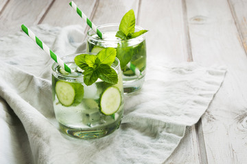 Summer refreshing detox cocktail with cucumber,mint and ice in glass on a white wooden background. Rustic.