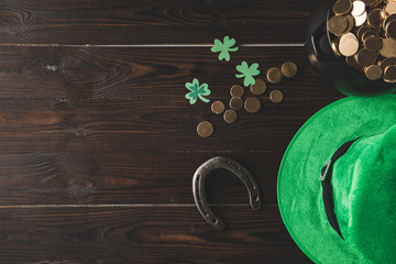 top view of pot with golden coins, horseshoe and green hat on wooden table, st patricks day concept