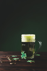 glass of beer with shamrock and golden coins on wooden table, st patricks day concept