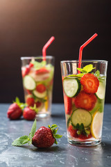 Cold and refreshing infused detox water with strawberry and cucumber in glass on black background.