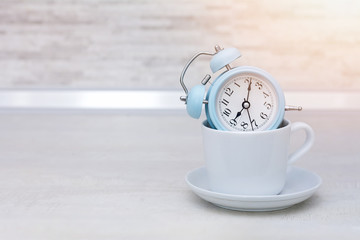 Alarm clock in coffee cup on the table, morning concept