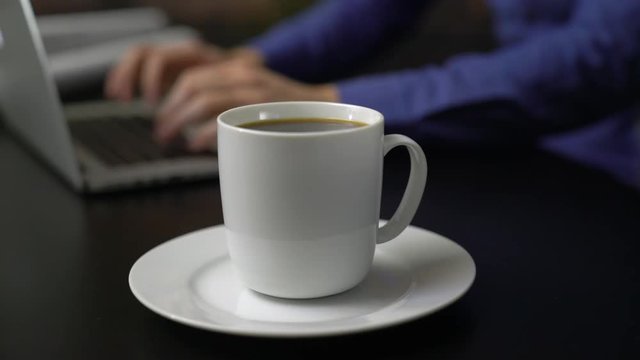 Hot mug of coffee near a man using laptop