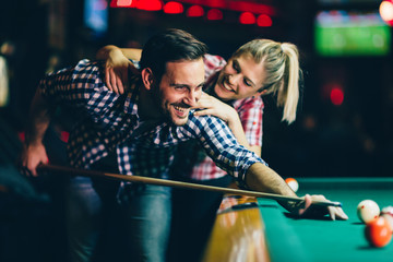 Young couple playing snooker together in bar - obrazy, fototapety, plakaty