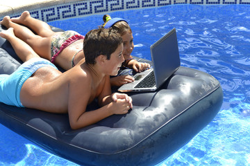 young boy and girl watching a movie on a partitive computer lap top  swimming in the pool on an inflatable mattress
