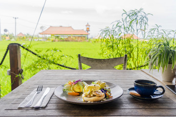 Breakfast with a view of the rice fields. Eggs Benedict and coffee. Side view with copy space