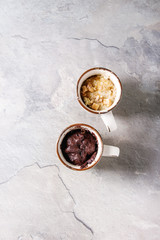 Chocolate and vanilla caramel mug cakes from microwave over grey texture background. Top view, copy space