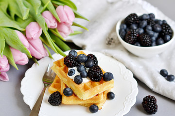 Homemade Belgian Waffles with Cream  Sauce Berries, Cup with Cappuccino Beverage Flowers Pink Tulips, Gray Background Table Kitchen, Towel White Plate, Spring Concept