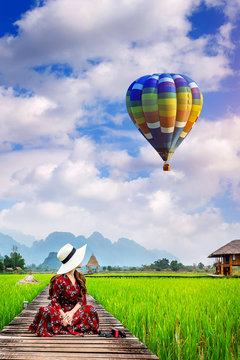 Young woman look at balloon and sitting on wooden path with green rice field in Vang Vieng, Laos.
