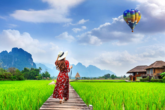 Young woman look at balloon and walking on wooden path with green rice field in Vang Vieng, Laos.