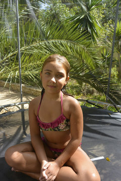Portrait of a girl in a bikini sitting in a lotus pose on a trampoline