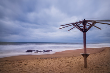 Deserted beach in off-season. Old umbrella on the shore and stones in the water. Gloomy sky. long exposure.
