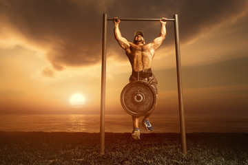 Strong man pulled on the bar at sunrise on the shores of lake