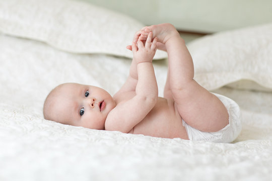 cute baby lying on white sheet and holding his legs