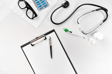 Stethoscope in the office of doctors.Top view of doctor's desk table, blank paper on clipboard with pen. Copy space. Designer's blank