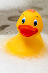 Toy plastic yellow duck floating in a bath surrounded by soap suds