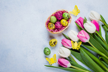 Easter Background with white and pink tulips and colorful quail eggs on blue stone table background. Spring Greeting card. Top view, flat lay, copy space.