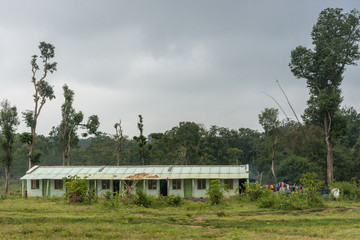 Fototapeta na wymiar Coorg, India - October 29, 2013: Dubare Elephant Camp. Green, public-housing, long-house with metal corrugated roof holds nine very small one-room dwellings. Gray sky, jungle environment. Laundry.