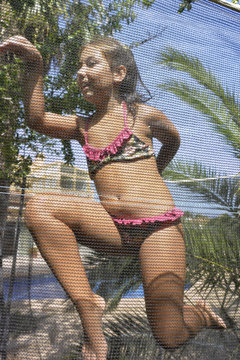 Happy young girl in bikini jumping on trampoline with different funny poses