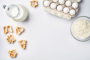 Wheat flour in the glass bowl, cream in a glass jar, chicken eggs - ingredients for the dough, top view
