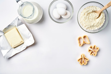 Objects and ingredients for baking, plastic molds for cookies on a white background. Flour, eggs, milk, butter, cream. Top view, space for text