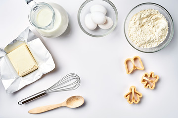 Objects and ingredients for baking, plastic molds for cookies on a white background. Flour, eggs, whisk, milk, butter, cream. Top view, space for text