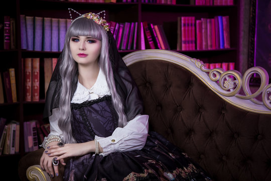 A beautiful woman in the form of lolita, dolls with cat ears sitting on the sofa in the library. Japanese street fashion.