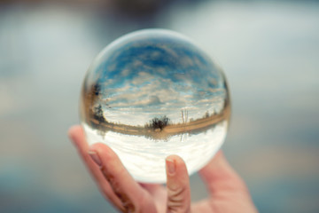 hand holding a glass ball with reflection of lake