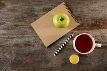 Cup of tea, apple and notebook on table, top view. Tasty breakfast