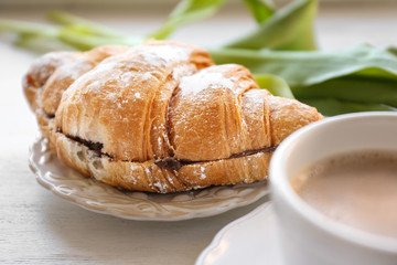 Plate with croissant and cup of coffee on table. Tasty breakfast