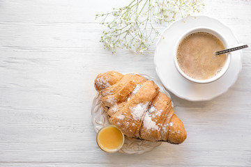 Plate with croissant and cup of coffee on table. Tasty breakfast