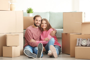 Young couple with moving boxes on floor in room