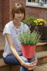 Mujer joven con plantas delante de su casa