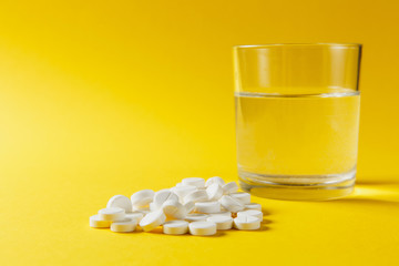 Medication pile white round tablets arranged abstract on yellow color background. Aspirin, glass...