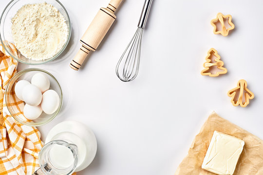 Objects And Ingredients For Baking, Plastic Molds For Cookies On A White Background. Flour, Eggs, Rolling Pin, Whisk, Milk, Butter, Cream. Top View, Space For Text