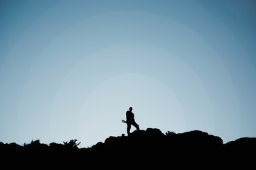 Man holding tripod and stand in top of peak hill in silhouette style with blue sky and radius. 