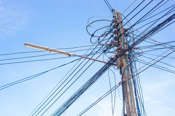 High voltage electricity pole and many wire of the cable line with blue sky and  lamp on the pole.