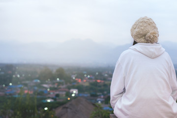 The Asian Girl wear white cloth and sitting the wood table. Looking at the villages with mountains...
