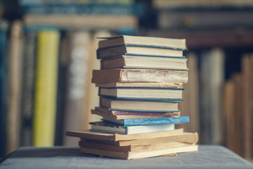 A stack of dusty shabby books in front of blurry shelves