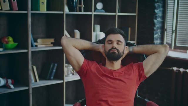 Successful businessman relaxing in cozy office. Portrait of young entrepreneur enjoying his new office. Bearded man relaxing on chair with hands behind head in work place