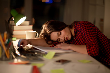 student or woman sleeping on table at night home