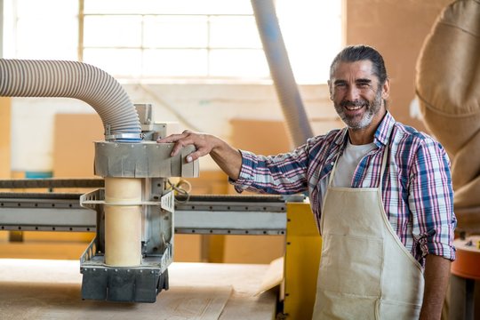Portrait of carpenter standing near engraving machine in the workshop