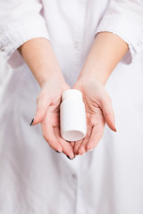 Slim young girl in white doctor's smock holds bottle with drugs, indoor isolated shot