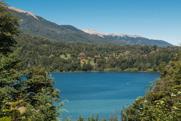 Landscape of a turquoise lake with houses in the background, trees and mountains