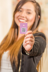 Close up of beautiful young woman showing a clothes ticket with QR code information, in a blurred background